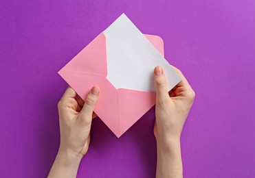 Photo of Woman holding envelope with blank invitation card on purple background, top view. Space for design