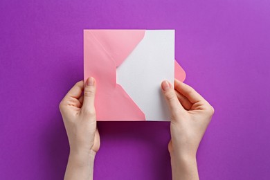 Photo of Woman holding envelope with blank invitation card on purple background, top view. Space for design