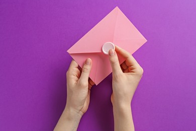 Photo of Woman holding beautiful invitation envelope with wax seal on purple background, top view