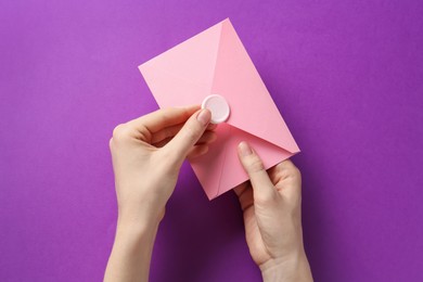 Photo of Woman holding beautiful invitation envelope with wax seal on purple background, top view