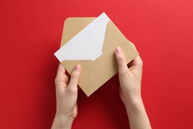 Photo of Woman holding envelope with blank invitation card on red background, top view