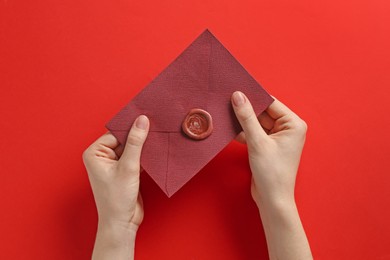 Photo of Woman holding beautiful invitation envelope with wax seal on red background, top view