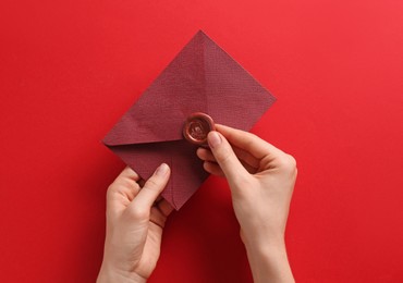 Photo of Woman holding beautiful invitation envelope with wax seal on red background, top view