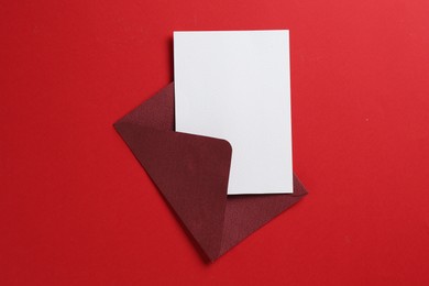 Photo of Blank invitation card and envelope on red background, top view. Space for design