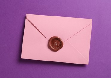 Photo of Beautiful invitation envelope with wax seal on purple background, top view