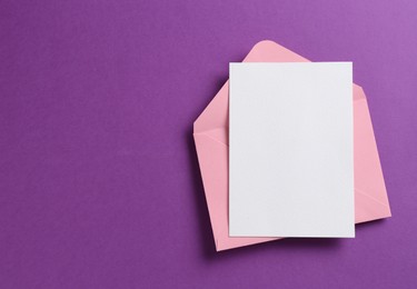 Photo of Blank invitation card and envelope on purple background, top view. Space for design