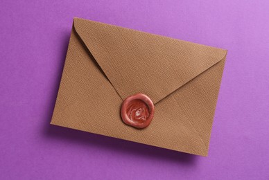 Photo of Beautiful invitation envelope with wax seal on purple background, top view
