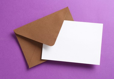 Photo of Blank invitation card and envelope on purple background, top view. Space for design
