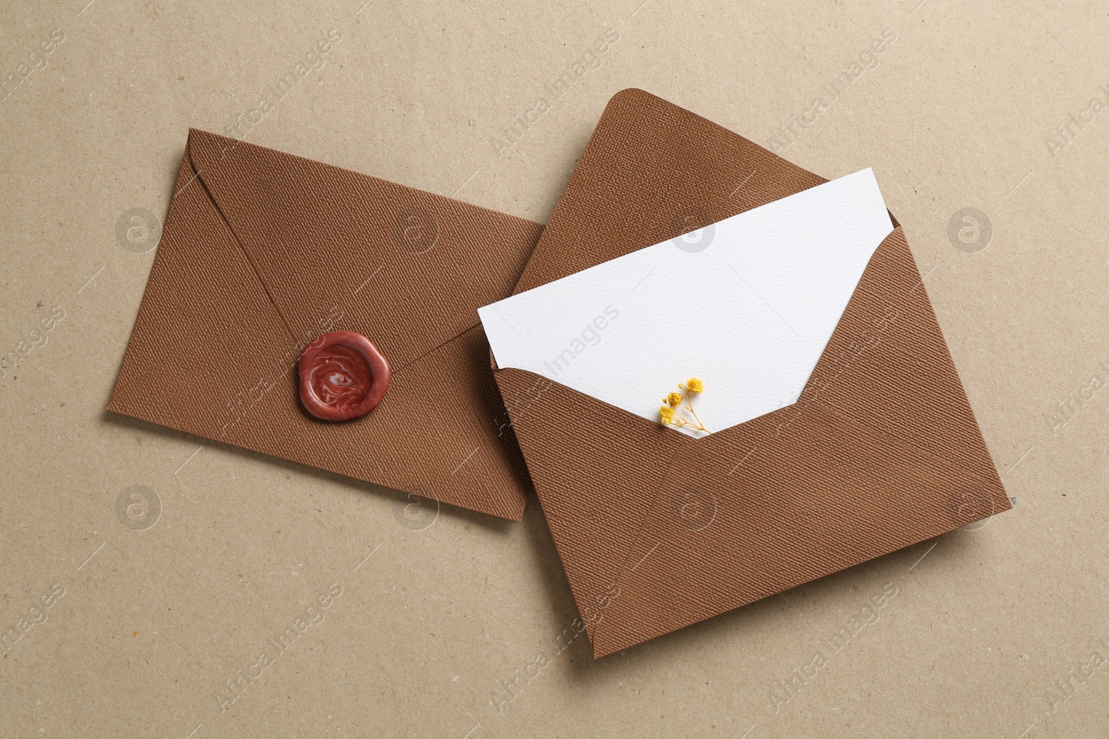 Blank invitation card with flowers and envelopes on carton, flat lay Photo of Blank invitation card with flowers and envelopes on carton, flat lay