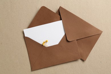 Photo of Blank invitation card with flowers and envelopes on carton, flat lay