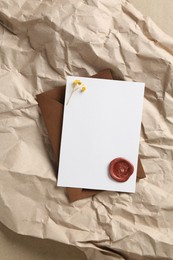 Photo of Blank invitation card with flowers, wax seal and envelope on parchment paper, top view. Space for design