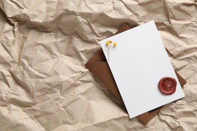 Photo of Blank invitation card with flowers, wax seal and envelope on parchment paper, top view. Space for design