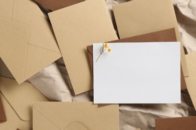Photo of Blank invitation card with flowers and envelopes on parchment paper, flat lay. Space for design