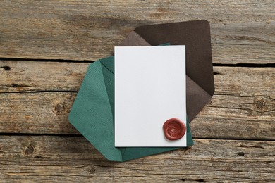 Photo of Blank invitation card with wax seal and envelope on wooden table, top view. Space for design