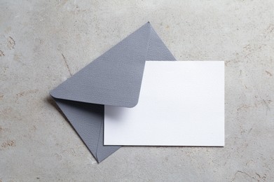 Photo of Blank invitation card and envelope on light grey table, top view. Space for design