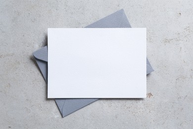 Photo of Blank invitation card and envelope on light grey table, top view. Space for design