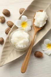 Photo of She butter, nuts and plumeria flowers on white wooden table, flat lay