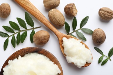 Photo of Shea butter, nuts and leaves on white background, flat lay