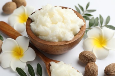 Photo of Shea butter, nuts, plumeria flowers and leaves on white background, closeup