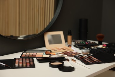 Photo of Different makeup products and brushes on dressing table indoors