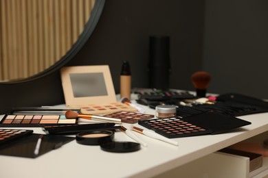 Photo of Different makeup products and brushes on dressing table indoors, closeup