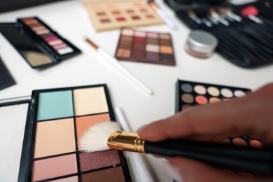 Photo of Woman with brush and correcting concealer palette at dressing table, closeup