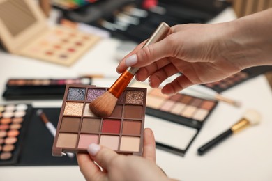 Photo of Woman with brush and eyeshadow palette at dressing table, closeup