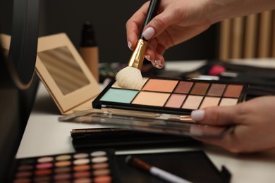 Photo of Woman with brush and correcting concealer palette at dressing table, closeup