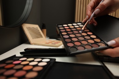 Photo of Woman with brush and eyeshadow palette at dressing table, closeup