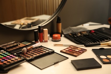Photo of Different makeup products and brushes on dressing table indoors, closeup
