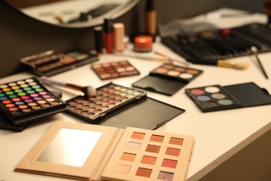 Photo of Different makeup products and brushes on dressing table indoors, closeup