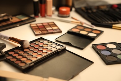 Photo of Different makeup products and brushes on dressing table indoors, closeup