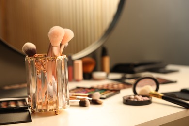 Photo of Different makeup products and brushes on dressing table indoors, closeup