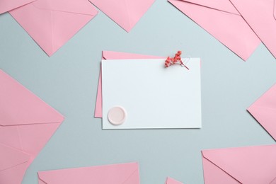 Photo of Blank invitation card with wax seal, flowers and envelopes on grey background, flat lay. Space for design