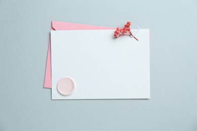 Photo of Blank invitation card with wax seal, flowers and envelope on grey background, top view. Space for design