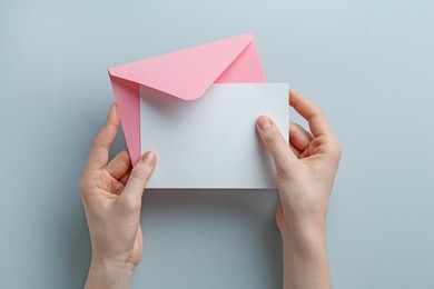Photo of Woman holding envelope with blank invitation card on grey background, top view. Space for design