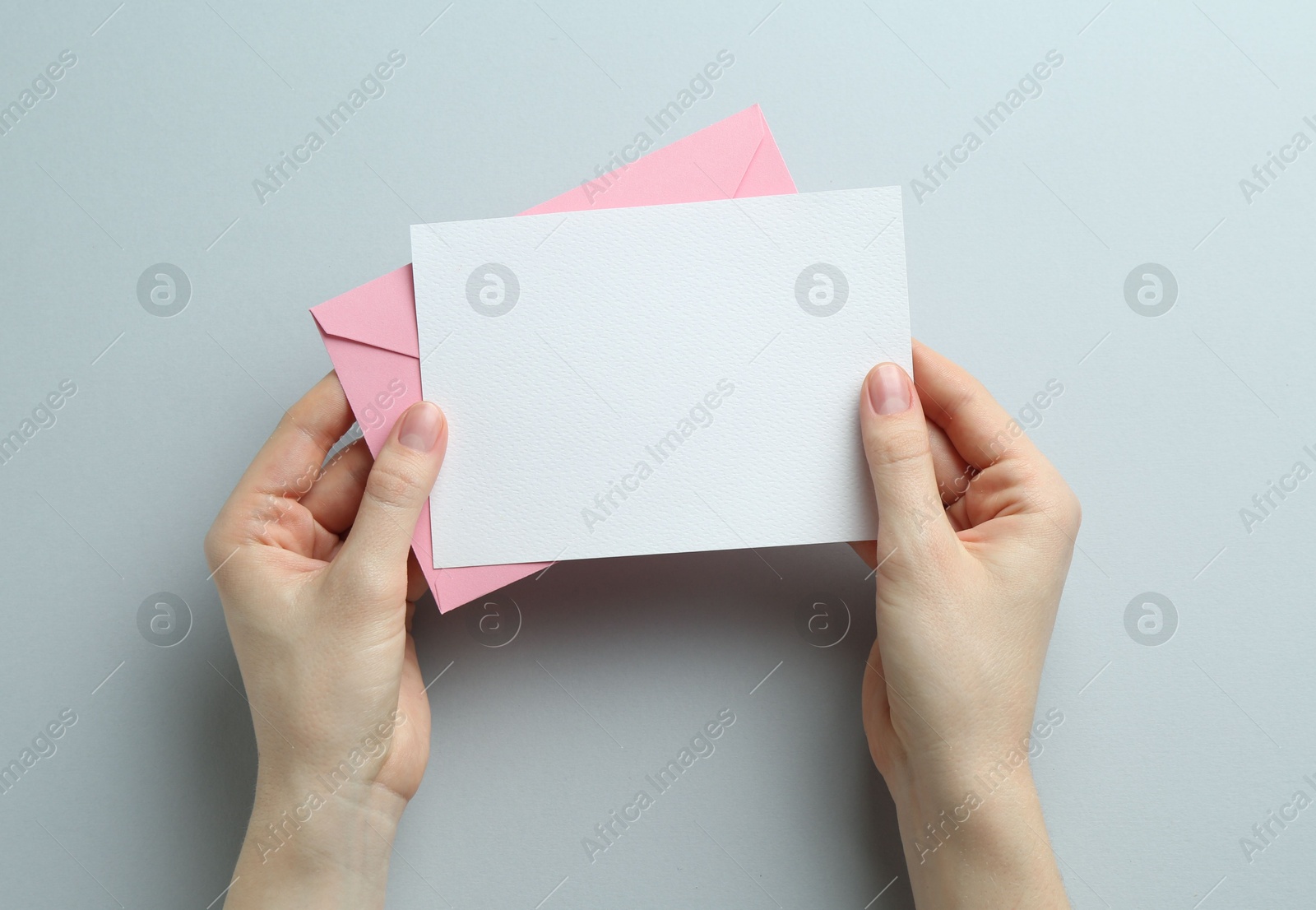 Woman holding envelope with blank invitation card on grey background, top view. Space for design Photo of Woman holding envelope with blank invitation card on grey background, top view. Space for design