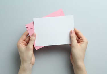 Photo of Woman holding envelope with blank invitation card on grey background, top view. Space for design