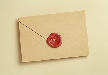 Photo of Beautiful invitation envelope with wax seal on beige background, top view