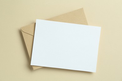 Photo of Blank invitation card and envelope on beige background, top view. Space for design