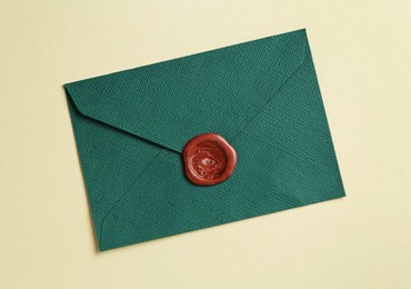 Photo of Beautiful invitation envelope with wax seal on beige background, top view