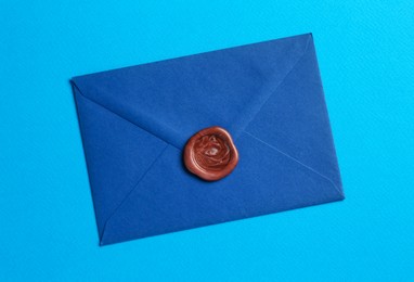 Photo of Beautiful invitation envelope with wax seal on light blue background, top view