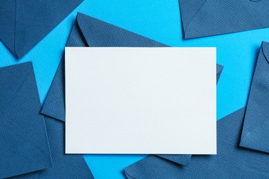 Photo of Blank invitation card and envelopes on light blue background, flat lay. Space for design