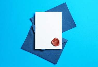 Photo of Blank invitation card with wax seal and envelopes on light blue background, flat lay. Space for design