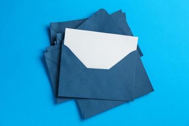 Photo of Blank invitation card and envelopes on light blue background, top view