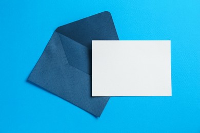 Photo of Blank invitation card and envelope on light blue background, top view. Space for design