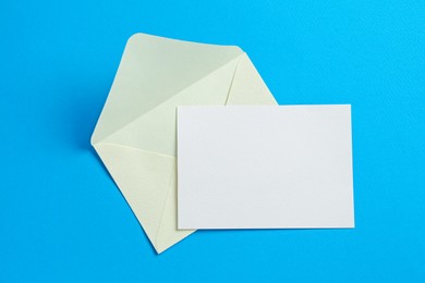Photo of Blank invitation card and envelope on light blue background, top view. Space for design