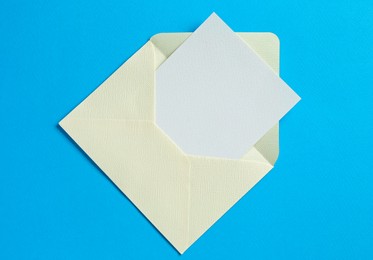 Photo of Blank invitation card and envelope on light blue background, top view. Space for design