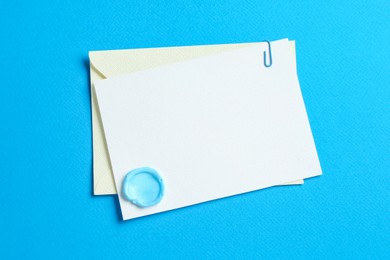 Photo of Blank invitation card with wax seal and envelope on light blue background, top view. Space for design