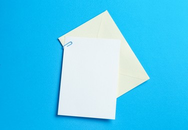 Photo of Blank invitation card and envelope on light blue background, top view. Space for design
